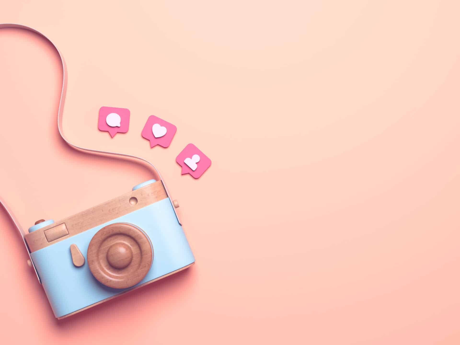  A blue toy camera with a brown strap and pink social media reactions on a pink background.